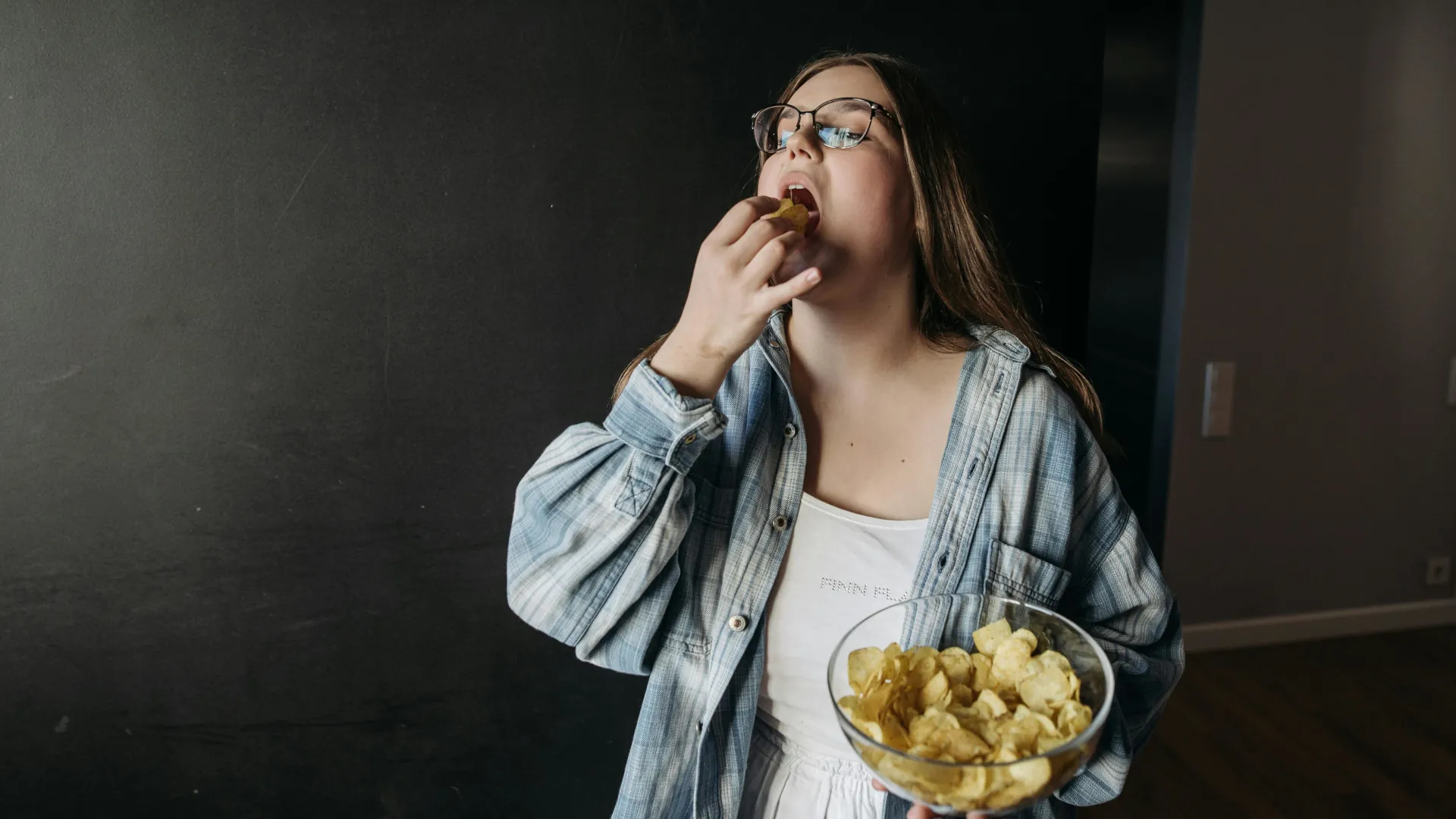 A young woman piles on an entire bowl of crisps, she has a food addiction.